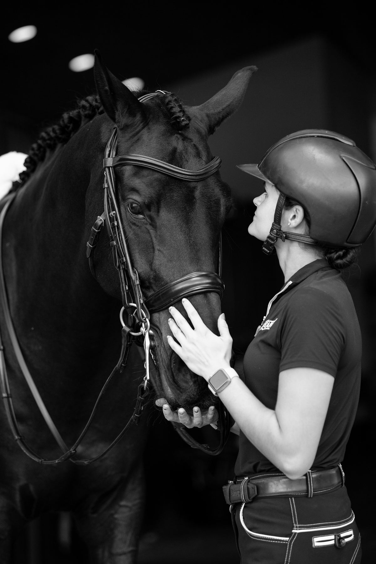 Woman in equestrian gear petting a horse in a stable.